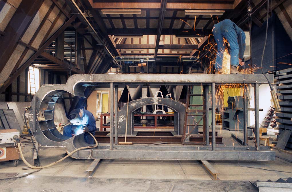 het stalen portaal horizontaal in het atelier. Er wordt tegelijkertijd aangelast en geslepen © André Boone