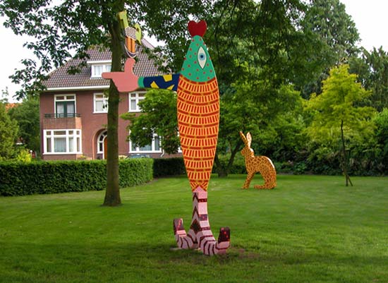 in de pastorietuin op de voorgrond een grote verticale vis getiteld De zalm van lugh. Op de achtergrond een haas met de schutskleuren van een giraf, getiteld Giraf © André Boone
