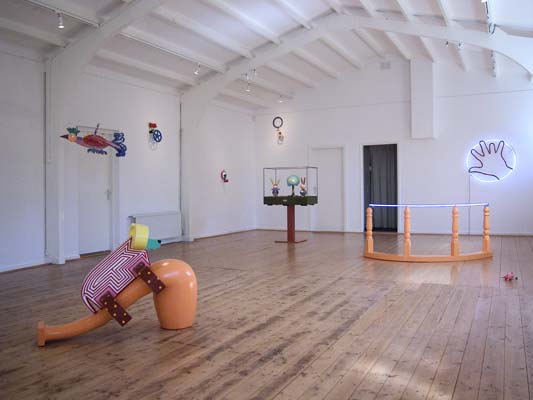het interieur van de galerie met oa beelden in de vorm van een monumentale gekleurde pijp met hierop een stier, een muziekbox van gekleurde hazen en een boom ingekaderd in een framewerk,©andré boone