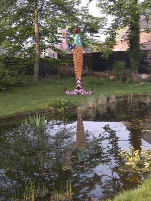 een gekleurde verticale vis met een horizontale uitgestrekte arm waarvan de hand de vorm heeft van een pistooltje, hierop staat een windvaan in de vorm van een schommelpaard